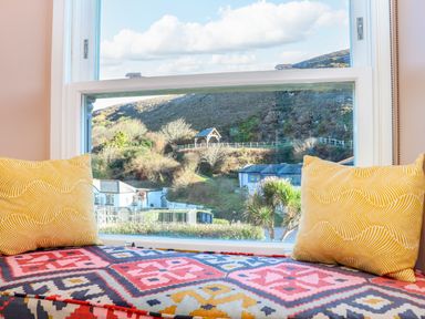 A window seat with patterned cushions and yellow pillows overlooking a hillside and houses at Mavericks Wave in St Agnes