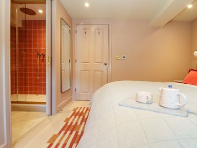 A bedroom with a bed and a tray holding a teapot and cup a doorway leading to a shower with red tiles and a wall mirror at Mavericks Wave in St Agnes