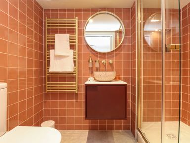 A bathroom with a toilet a towel rack with towels a round mirror a sink with a cabinet and a glass shower enclosure at Mavericks Wave in St Agnes
