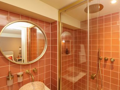 A bathroom with terracotta tiled walls a round mirror a vessel sink and a glass shower enclosure at Mavericks Wave in St Agnes