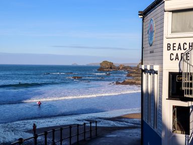 A beach with a surfer in the water and a building labeled beach cafe at Mavericks Wave in St Agnes