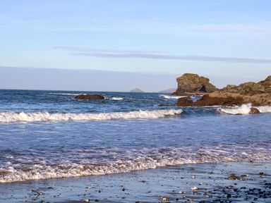 A beach with waves washing onto shore and rocky formations in the sea at Mavericks Wave in St Agnes