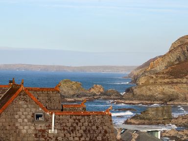 A coastal scene with rocky cliffs and tiled rooftops near the ocean at Mavericks Wave in St Agnes