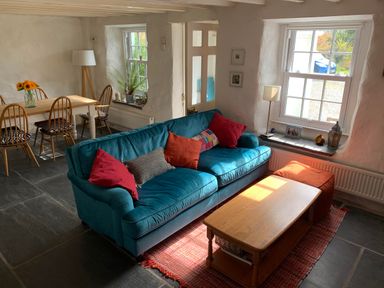 A living room with a blue sofa and coffee table next to a dining table with four chairs at Kernyk in Carn Brea near Pool