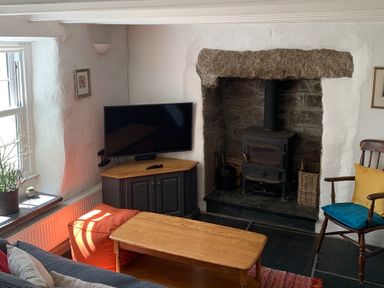 A living room with a wood stove fireplace television on a cabinet wooden coffee table and chair with cushions at Kernyk in Carn Brea near Pool