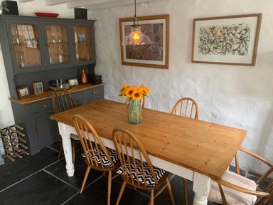 A dining room with a wooden table and six chairs a glass vase with sunflowers two framed pictures on a white wall and a dark gray cabinet with glass doors at Kernyk in Carn Brea near Pool