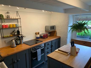 A kitchen with wooden countertops blue cabinets a microwave toaster kettle hanging plant and shelves with cups at Kernyk in Carn Brea near Pool