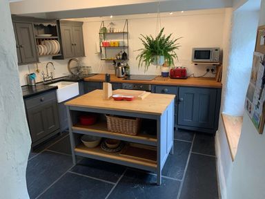 A kitchen with gray cabinets a wooden countertop a hanging plant and a kitchen island at Kernyk Carn Brea near Pool