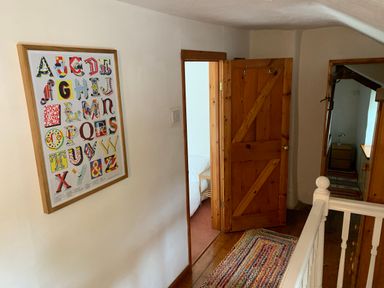A hallway with a framed alphabet poster on the wall a wooden door open to a bedroom and a multicolored rug on the wooden floor at Kernyk in Carn Brea near Pool