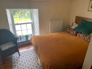 A bedroom with a double bed with orange bedspread a wicker chair by a window and a radiator at Kernyk Carn Brea near Pool