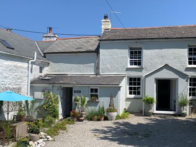 A white stone house with multiple windows and chimneys with gravel in the front and potted plants with a blue umbrella at Kernyk in Carn Brea near Pool