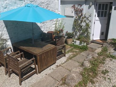 An outdoor seating area with a wooden table and chairs under a blue umbrella near a white door at Kernyk in Carn Brea near Pool
