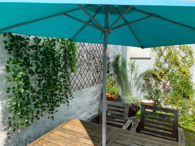 An outdoor seating area with wooden table and chairs under a blue umbrella with plants on lattice panels at Kernyk in Carn Brea near Pool