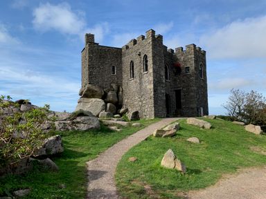 A stone castle on a grassy hill with a gravel path and rocks at Kernyk in Carn Brea near Pool