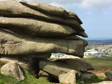 A large rock formation overlooking a town and green fields at Kernyk in Carn Brea near Pool