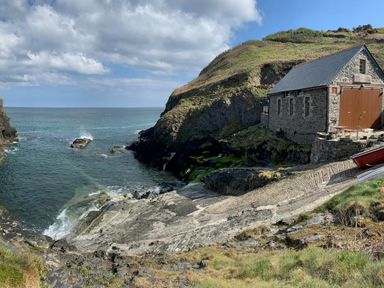 A stone boathouse by a rocky shoreline with a small cove and the sea at Kernyk in Carn Brea near Pool