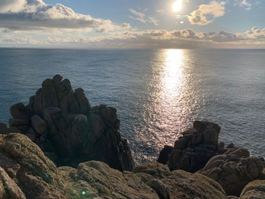 Rocky cliffs overlooking calm sea water with sun reflecting on the surface at Kernyk in Carn Brea near Pool