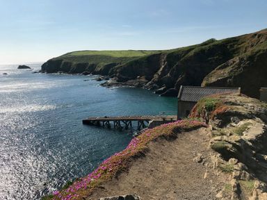 A coastal cliff with a wooden dock and a building near the water at Kernyk Carn Brea near Pool
