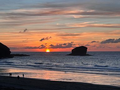 A beach with people on the shore at sunset with rock formations in the sea at Kernyk in Carn Brea near Pool