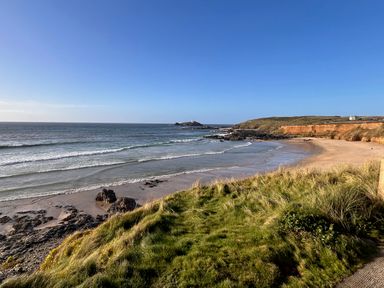 A coastal beach with grassy cliffs and rocky shoreline at Kernyk in Carn Brea near Pool