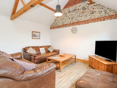 A living room with brown leather sofas a wooden coffee table a television on a wooden cabinet and a clock on the wall at The Old Dairy in Tittleshall near Brisley