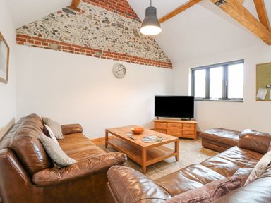 A living room with brown leather sofas a wooden coffee table and a television at The Old Dairy in Tittleshall near Brisley