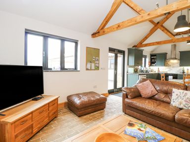 A living room with a brown leather sofa and ottoman a wooden TV stand with a television and a wooden coffee table at The Old Dairy in Tittleshall near Brisley
