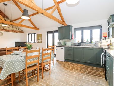A kitchen and dining area with wooden chairs and a table with a polka dot tablecloth at The Old Dairy in Tittleshall near Brisley
