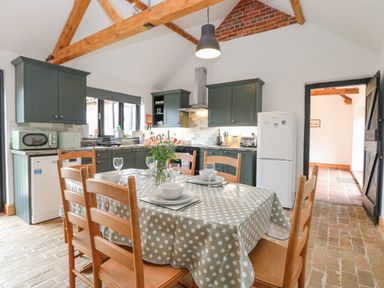 A kitchen with wooden chairs around a dining table with polka dot tablecloth and green cabinets at The Old Dairy in Tittleshall near Brisley