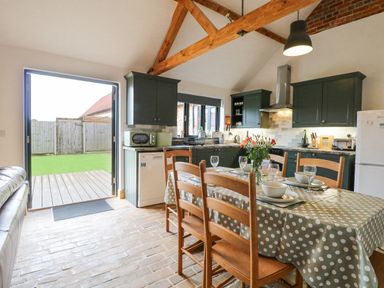 A kitchen with a dining table with chairs and kitchen cabinets with appliances at The Old Dairy in Tittleshall near Brisley