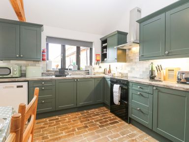 A kitchen with green cabinets brown brick floor and a window above the sink at The Old Dairy in Tittleshall near Brisley