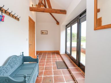A hallway with terracotta tiled floor wooden door bench coat hooks and glass doors at The Old Dairy in Tittleshall near Brisley