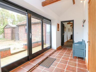 A hallway with large glass doors on one side and a blue wooden bench against the wall at The Old Dairy in Tittleshall near Brisley
