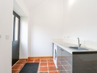 A utility room with tiled floor a black door a countertop with a sink and a washing machine at The Old Dairy in Tittleshall near Brisley