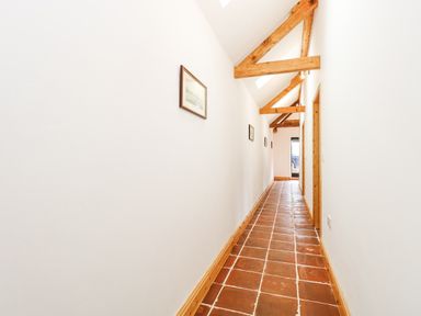 A long narrow hallway with terracotta tile flooring wooden ceiling beams and framed pictures on the wall at The Old Dairy in Tittleshall near Brisley