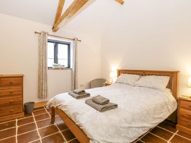 A bedroom with a wooden bed and dresser two bedside tables with lamps curtains on window and tiled floor at The Old Dairy in Tittleshall near Brisley