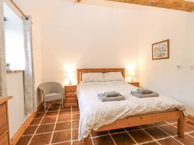 A bedroom with a wooden bed with white bedding two bedside tables with lamps a chair and a window at The Old Dairy in Tittleshall near Brisley