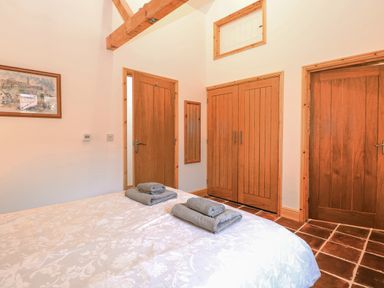 A bedroom with a bed with folded towels on it and wooden doors with a framed picture on the wall at The Old Dairy in Tittleshall near Brisley