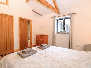 A bedroom with a bed, chest of drawers, window with curtains, and wooden doors at The Old Dairy in Tittleshall near Brisley
