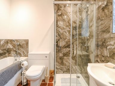 A bathroom with a toilet, bathtub, shower enclosure, and sink with marble patterned tiles at The Old Dairy in Tittleshall near Brisley