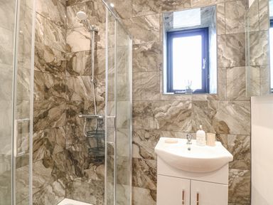 A bathroom with a shower enclosure and a sink under a window at The Old Dairy in Tittleshall near Brisley