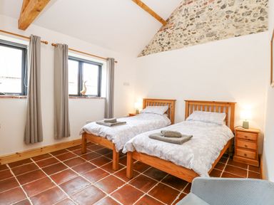 A bedroom with two single beds two windows and a stone accent wall at The Old Dairy in Tittleshall near Brisley