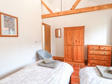 A bedroom with two beds blue chair wooden wardrobe and chest of drawers at The Old Dairy in Tittleshall near Brisley