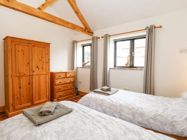 A bedroom with two single beds wooden wardrobe wooden chest of drawers and two windows with curtains at The Old Dairy in Tittleshall near Brisley