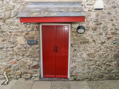 A red double door entrance with black handles under a small roof on a stone wall at Wood Cottage in Solva