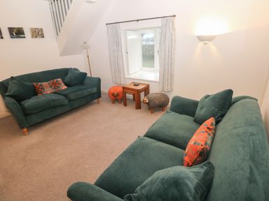 A living room with two green sofas two small wooden tables and animal shaped stools at Wood Cottage in Solva