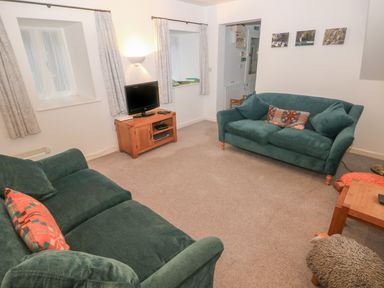 A living room with green sofas a wooden TV stand and small wall pictures at Wood Cottage in Solva
