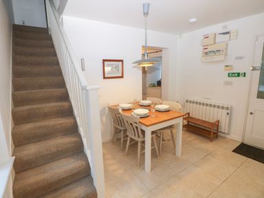 A dining area with a table set for four next to a carpeted staircase and an exit door at Wood Cottage in Solva