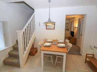 A dining area with a wooden table set for four next to a staircase leading upstairs at Wood Cottage in Solva