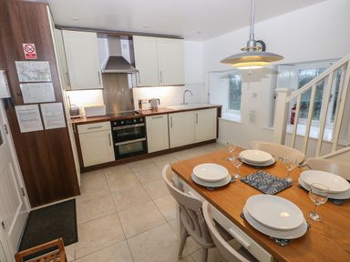 A kitchen with white cabinets and wooden countertops next to a dining table set with plates and glasses at Wood Cottage in Solva